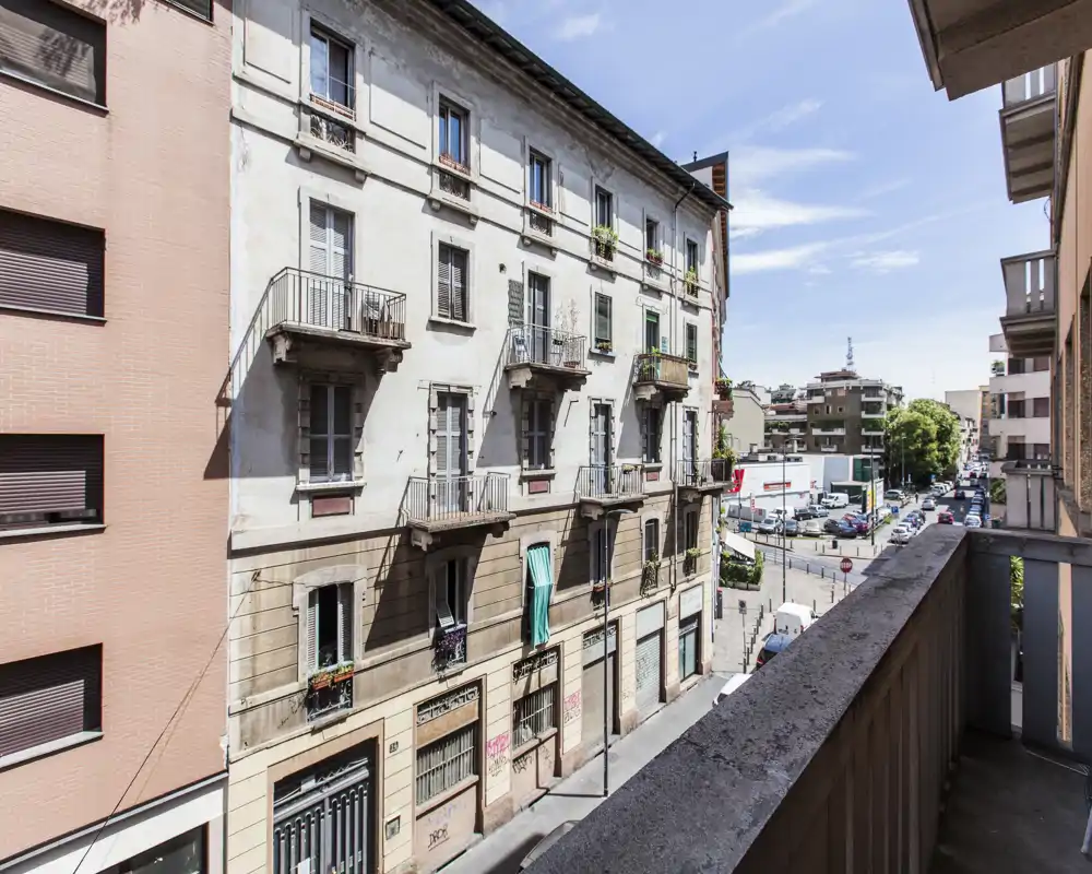 Balcone soleggiato con vista su una strada residenziale e sull'edificio adiacente; perfetto per un caffè mattutino con cielo limpido e vedute urbane.