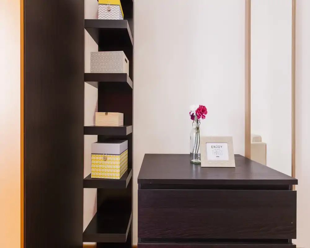 Angolo d'ingresso ordinato con mobili contenitori in legno scuro, scatole decorative e un piccolo vaso con fiori sopra, che crea una buona prima impressione.