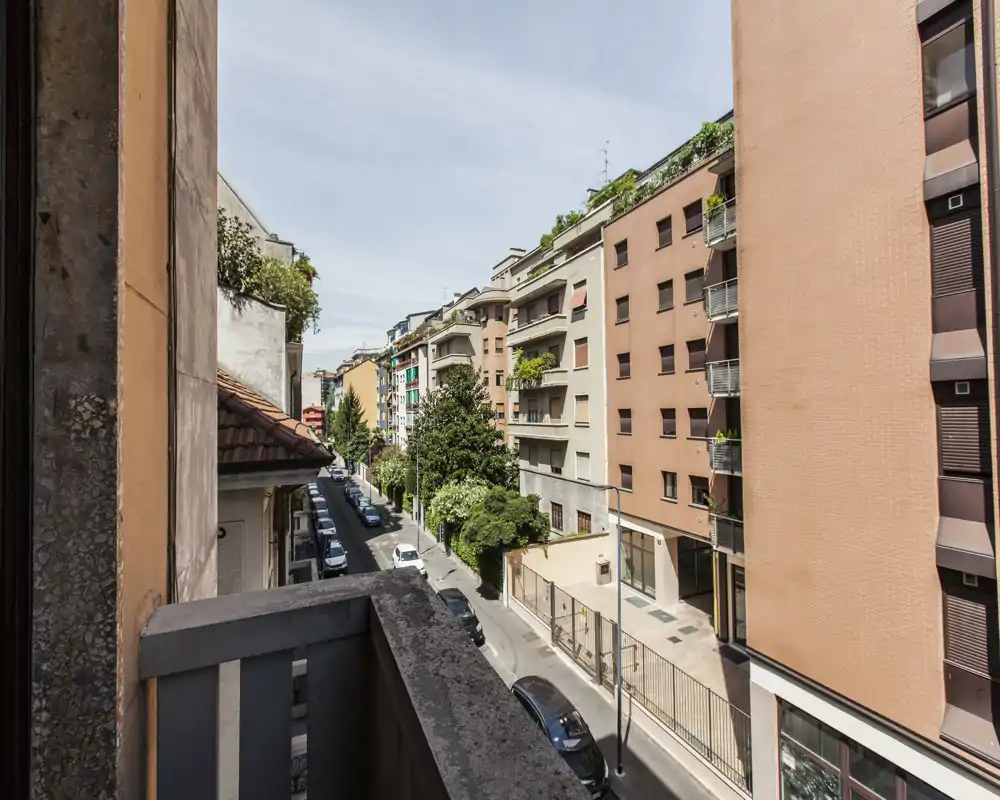 Balcone soleggiato con vista su una tranquilla via residenziale, palazzi e auto parcheggiate — perfetto per il caffè mattutino e osservare la città.