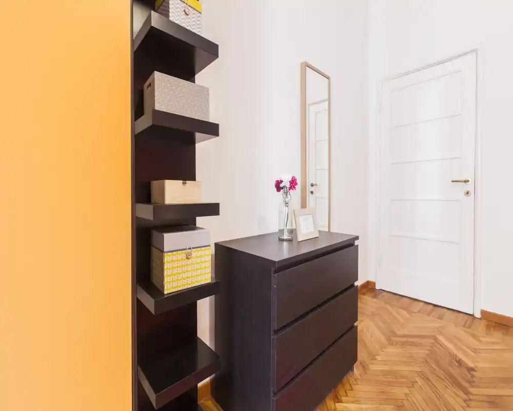 Ingresso luminoso e minimalista con cassettiera scura, mensole a parete con scatole decorative, specchio a figura intera e pavimento in parquet — prima impressione pulita e accogliente.