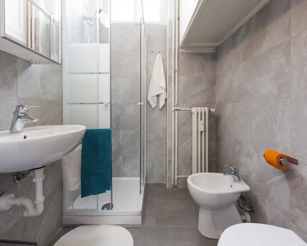 Bagno compatto e pulito con cabina doccia, lavabo, bidet e piastrelle grigie neutre; luminoso, ben illuminato e funzionale per soggiorni.