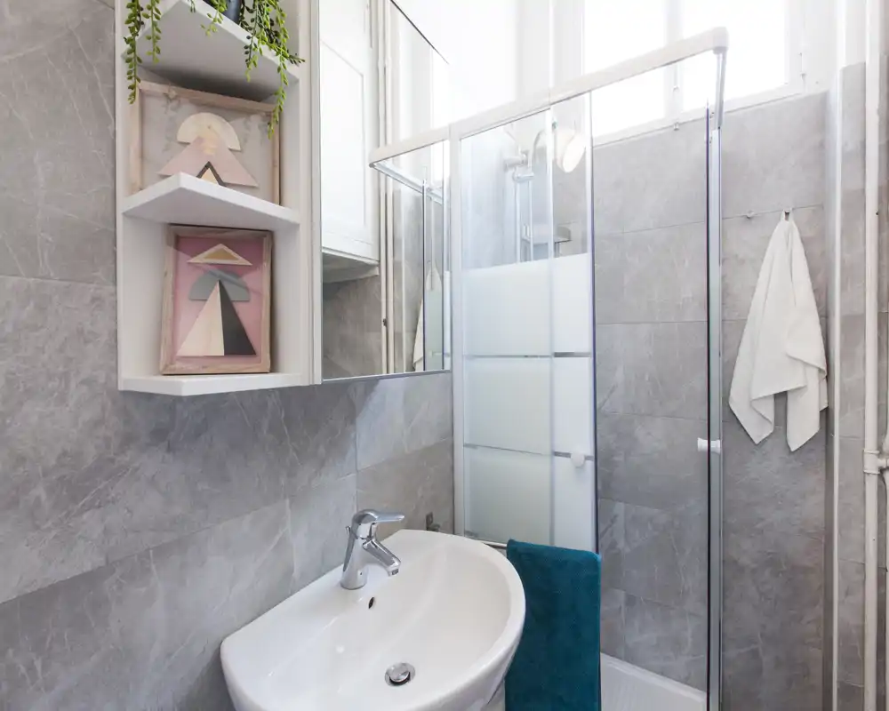 Bagno moderno e luminoso con lavabo bianco, box doccia in vetro e pareti piastrellate grigie; compatto e ben curato.