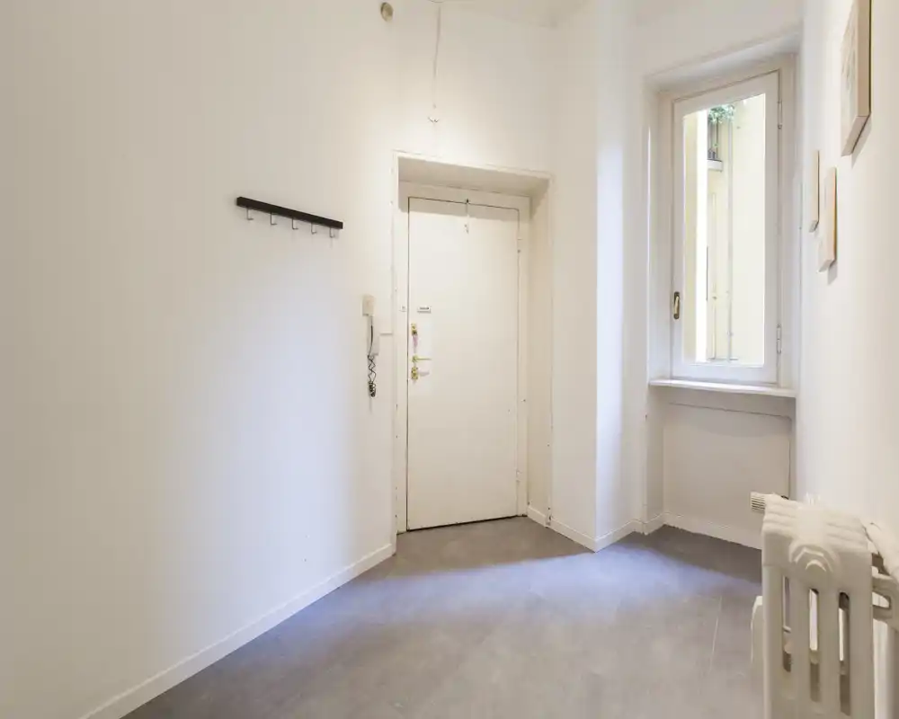 Ingresso piccolo e pulito con porta bianca, finestra che porta luce naturale e un attaccapanni a parete — spazio neutro e ordinato ideale per l’entrata di un appartamento.