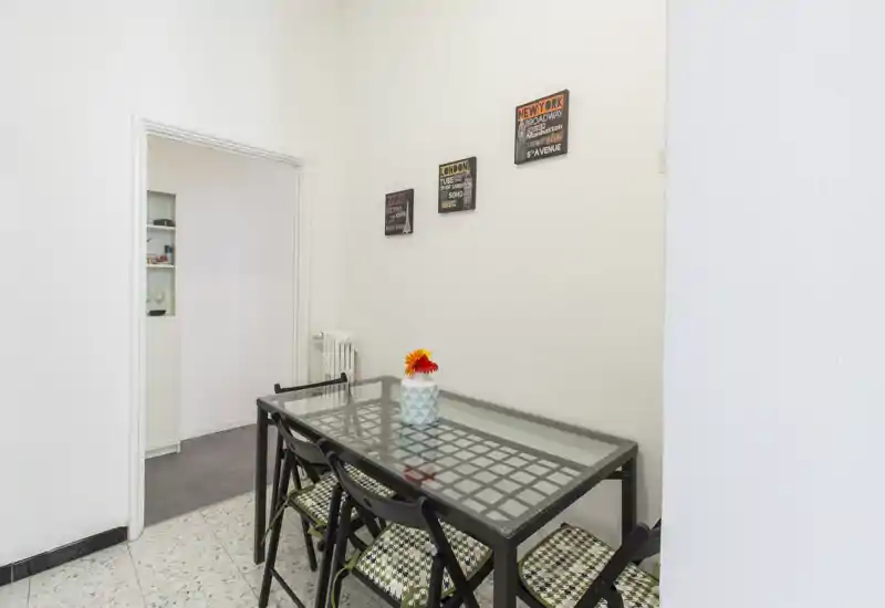 Compact dining area with a glass-topped table, four foldable chairs with patterned cushions and a decorative vase; bright, tidy and suitable for a small apartment.