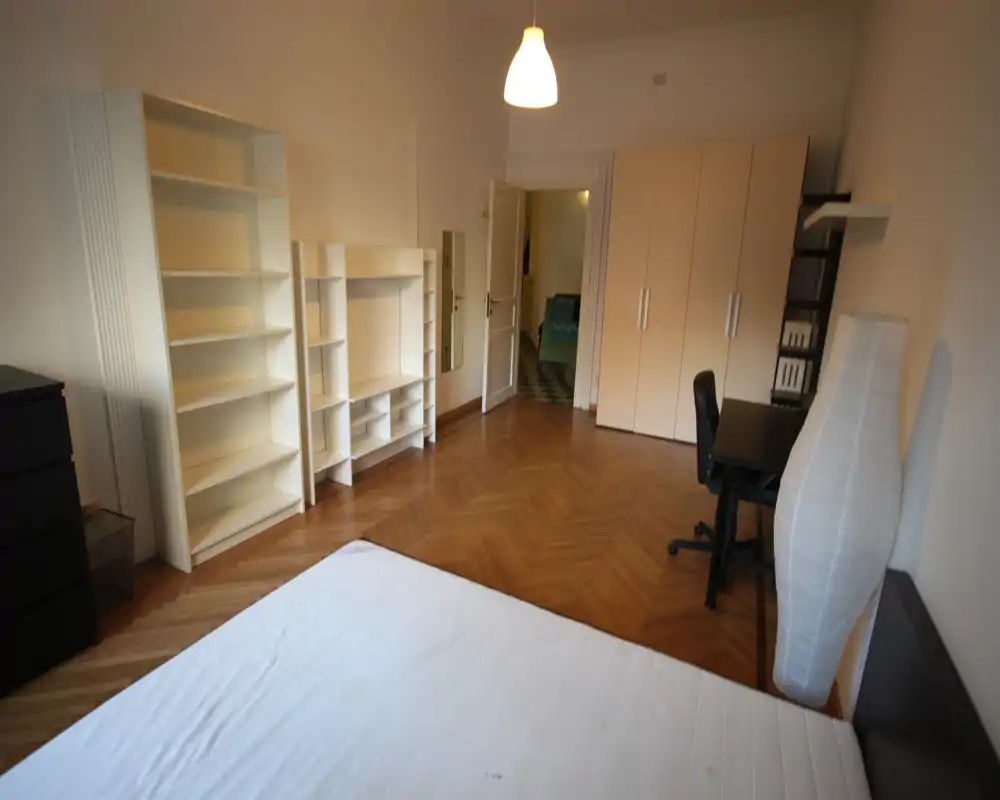 Dormitorio minimalista y bien iluminado con colchón en primer plano, armario y estanterías en las paredes, escritorio y silla — ideal para alquiler individual o de estudiantes.