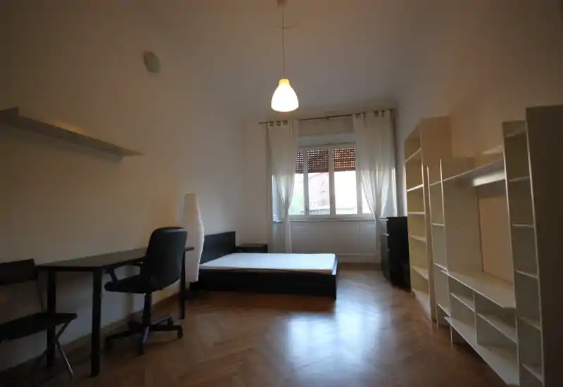 Dormitorio amplio y luminoso con somier doble, escritorio y estanterías; gran ventana con cortinas y bonito suelo de parquet.