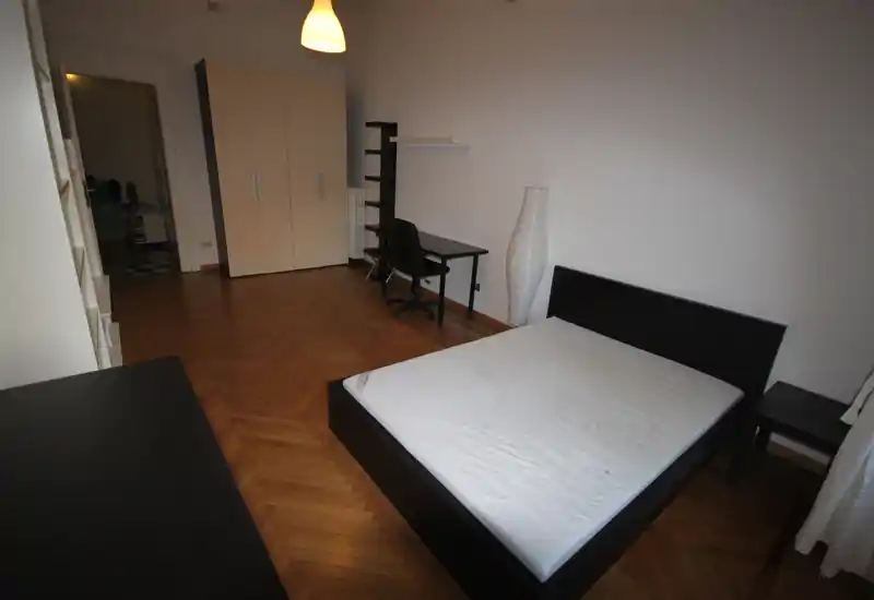 Amplio dormitorio con cama doble en estructura baja negra, suelo de parquet, armario y pequeño escritorio: sencillo, moderno y bien encuadrado para un anuncio.