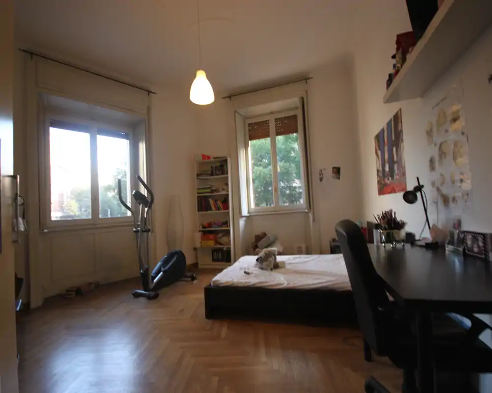 Dormitorio amplio y luminoso con cama baja, grandes ventanas con luz natural, escritorio y estantería — cómodo para estudiante o ocupante individual.