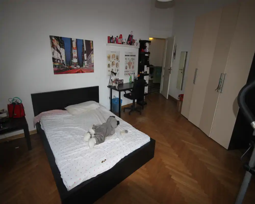 Amplio dormitorio con cama doble, suelo de parquet, armario y pequeño escritorio de estudio. Paredes neutras y decoración sencilla, apto para anuncios de alquiler.