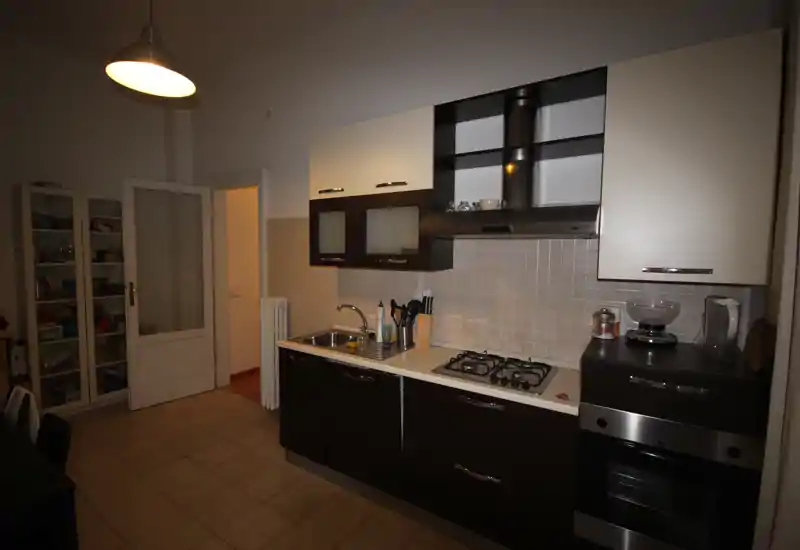 Cucina a corridoio ben attrezzata con mobili bassi scuri e pensili chiari, piano cottura a gas, forno incassato, lavello e scaffalature aperte — disposizione pratica per la cucina di tutti i giorni.