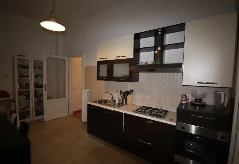 Cucina moderna con pensili chiari e basi scure, piano cottura a gas, forno incassato e lavello in acciaio. Il rivestimento a piastrelle e le mensole aperte offrono spazio pratico e un aspetto ordinato.