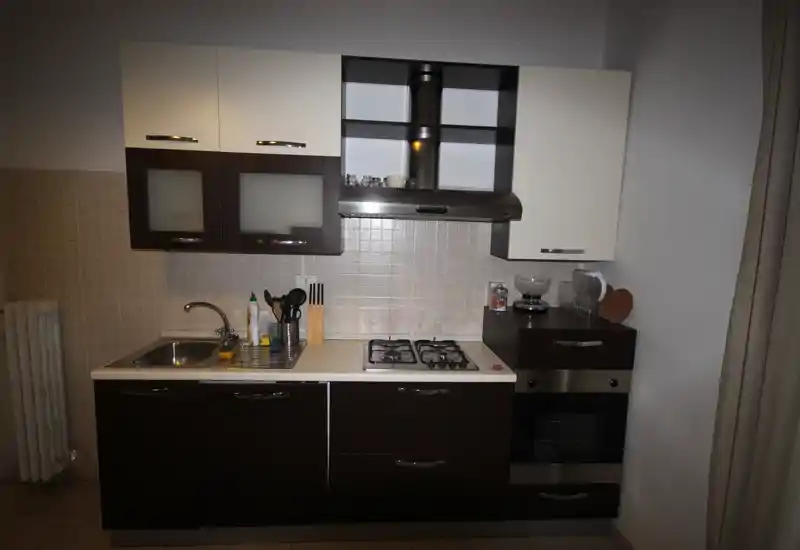 Cucinotto moderno e compatto con basi scure e pensili chiari, lavello in acciaio, piano cottura a gas a quattro fuochi e forno incorporato — layout pratico per un piccolo appartamento.