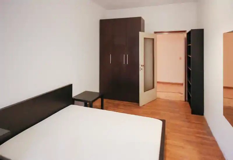 Dormitorio luminoso y amueblado de forma sencilla con una cama grande, cabecero y armario de madera oscura. Suelo de madera cálido y líneas limpias para un espacio funcional ideal para alquileres.