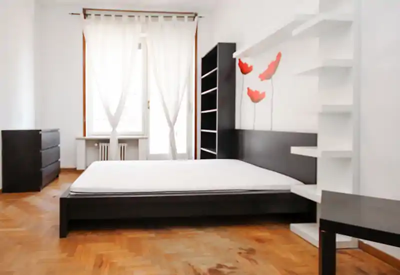 Bright, modern bedroom with a large low-profile bed, minimalist dark wood furniture and natural light from a window with sheer curtains.