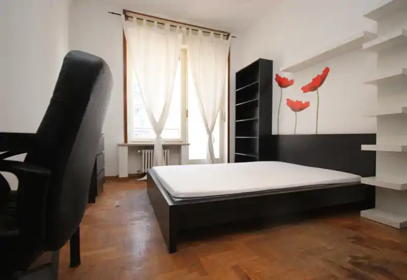 Bright, minimal bedroom with a low dark wood bed frame, large window with sheer curtains, and shelving. Clean lines and natural light make it suitable for rental photos.