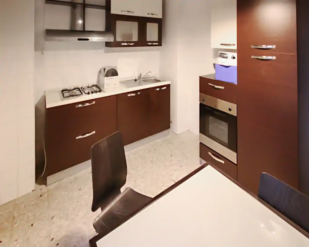 Cocina moderna y compacta con muebles oscuros, placa de gas, horno empotrado y una pequeña mesa. Distribución práctica y bien iluminada, perfecta para un piso pequeño.