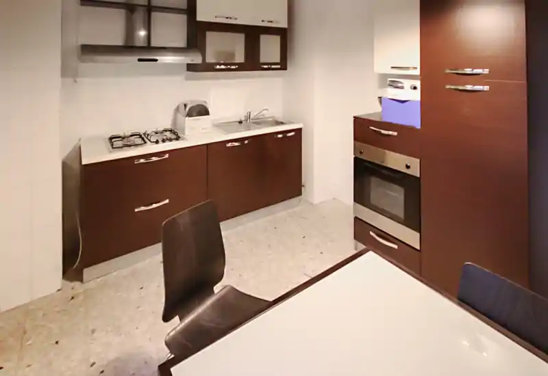 Compact modern kitchen with dark cabinets, gas hob, built-in oven and a small dining table. Well-lit practical layout ideal for a small apartment.