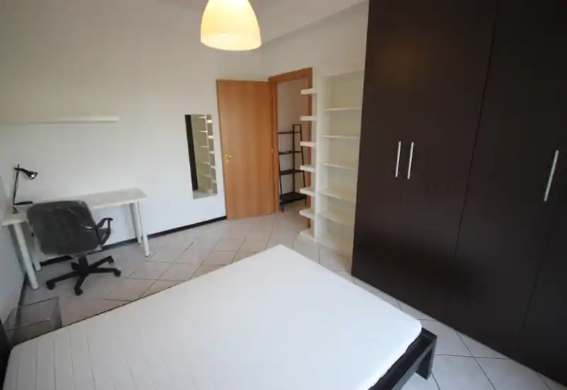 Chambre lumineuse et sobrement meublée avec lit double, grand placard et bureau. Sol carrelé et étagères offrant des rangements pratiques.