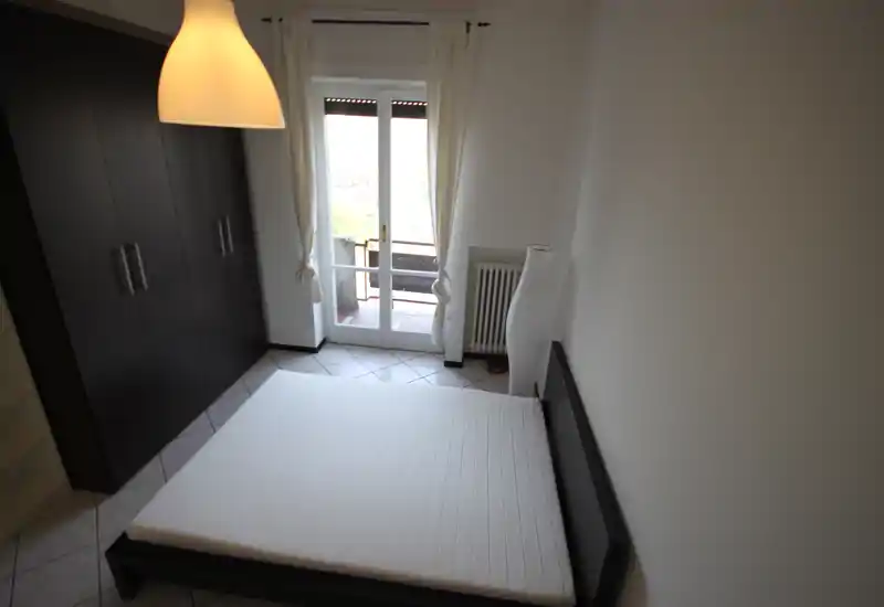 Chambre lumineuse et minimaliste avec un lit bas double, une grande armoire et une porte-fenêtre donnant sur le balcon. Lignes épurées et décoration neutre créent une atmosphère apaisante.