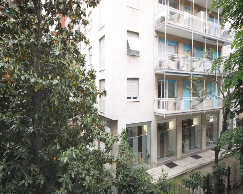 Vista della facciata di un edificio e alberi vicini ripresa da un balcone; la vegetazione in primo piano offre privacy e una vista urbana tranquilla.