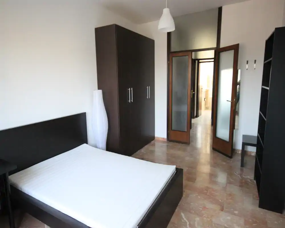 Camera da letto luminosa e minimale con letto matrimoniale, armadio in legno scuro e pavimento in marmo. Arredamento moderno e pulito, ideale per annunci.