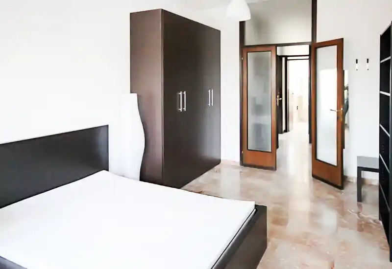 Camera da letto luminosa e moderna con grande letto matrimoniale, armadio scuro e pavimento in marmo — stile minimal e pulito, perfetto per annunci.