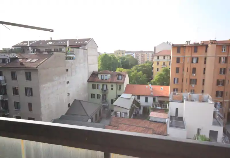 Vista dal balcone sulle tegole dei palazzi vicini e un piccolo cortile con alberi; panorama urbano con buona luce naturale.