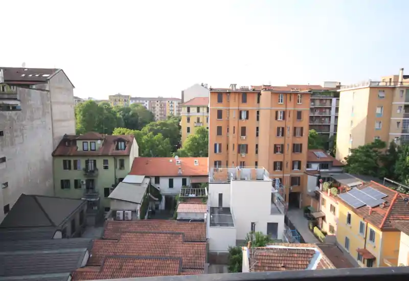 Ampia vista esterna da un piano alto con tetti dei palazzi vicini, edifici e chiome d'alberi — adatta a illustrare una terrazza o un balcone.