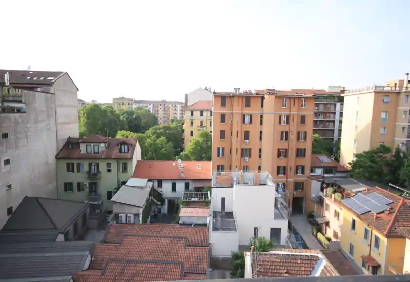 Vista sui tetti e sul cortile cittadino da una finestra/terrazzo che mostra edifici vicini, alberi e luce diurna, ideale per evidenziare la posizione e il contesto.