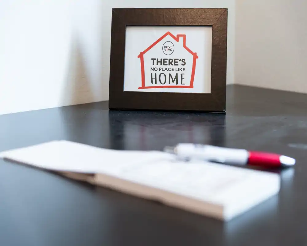 Close-up of a dark tabletop with a framed decorative sign, a pen and blurred paper — no clear room context visible.