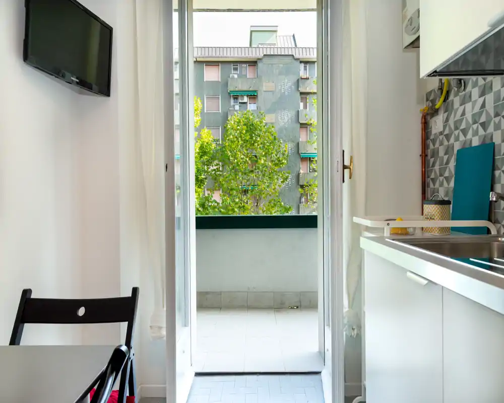 Compact kitchenette with a sink, patterned backsplash and an open doorway to a small balcony that brings abundant natural light.