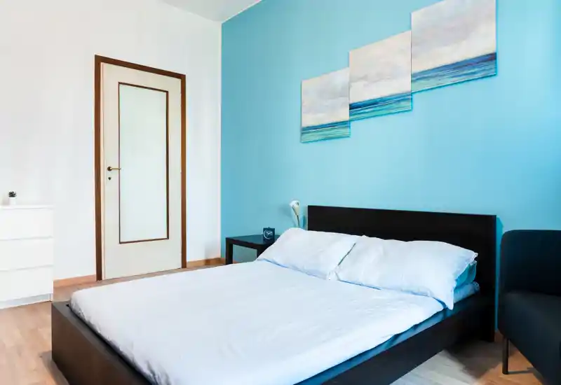 Bright, modern bedroom with a low dark wood bedframe, white linens and coastal artwork on a soothing blue accent wall — clean, airy and simply styled for comfortable stays.
