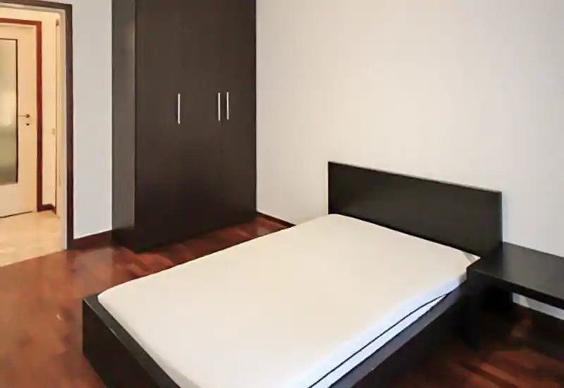 Chambre moderne et épurée avec un lit bas double, une tête de lit en bois foncé et une table de chevet assortie. Placard minimal et parquet chaleureux pour un espace de nuit contemporain.