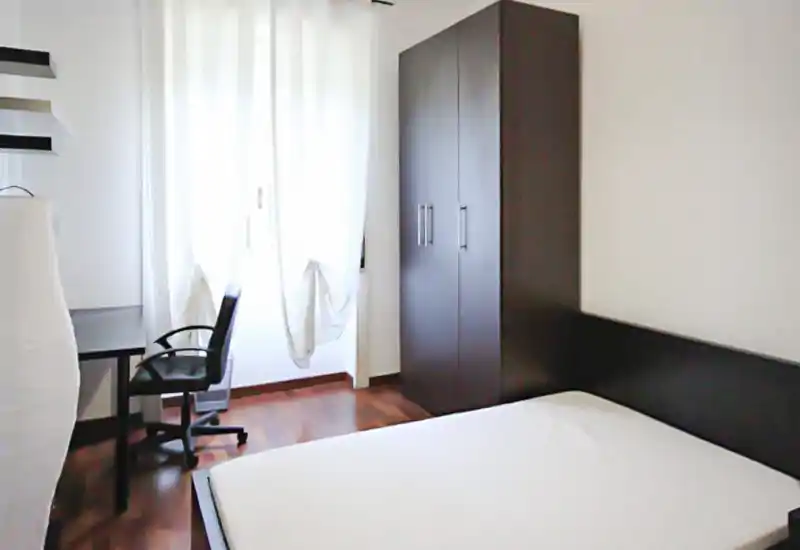 Chambre lumineuse et épurée avec lit double, tête de lit et armoire foncés, parquet et bureau près de la fenêtre apportant une belle lumière naturelle.