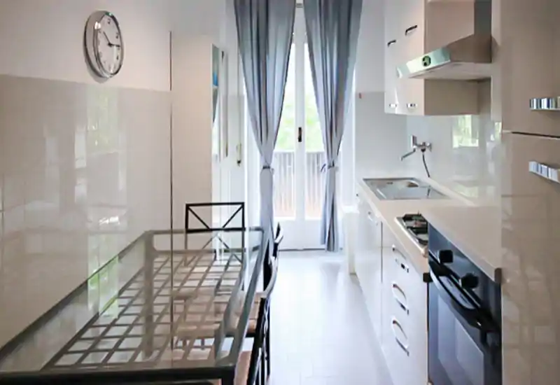 Cuisine moderne et lumineuse avec table en verre, four encastré, évier et porte-fenêtre donnant sur le balcon — idéale pour un appartement citadin compact.