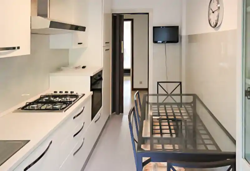 Cuisine en enfilade moderne avec placards blancs, four encastré et plaque à gaz, table à plateau en verre et chaises — lumineuse, fonctionnelle et bien rangée.