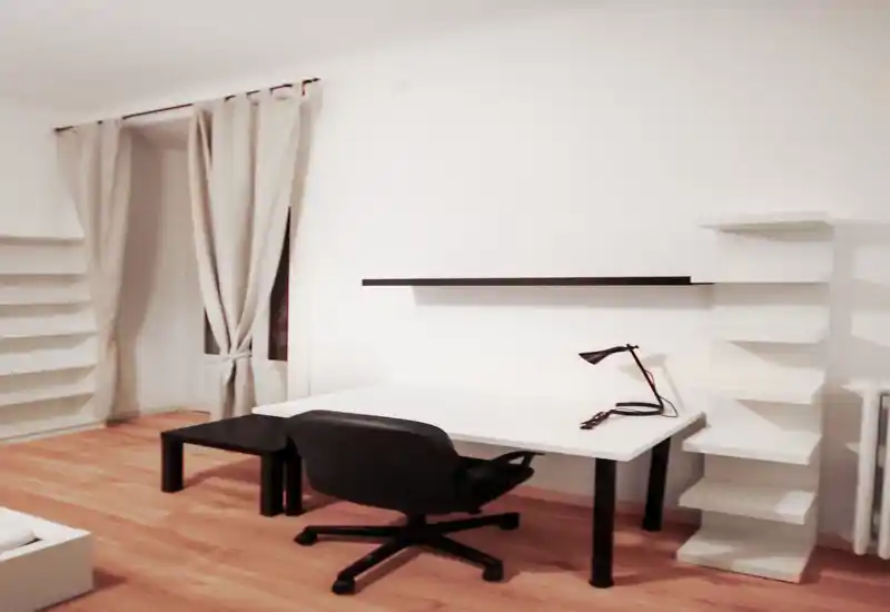 Minimal, well-lit living area with a desk, office chair and shelving — clean Scandinavian-style workspace within a living room.