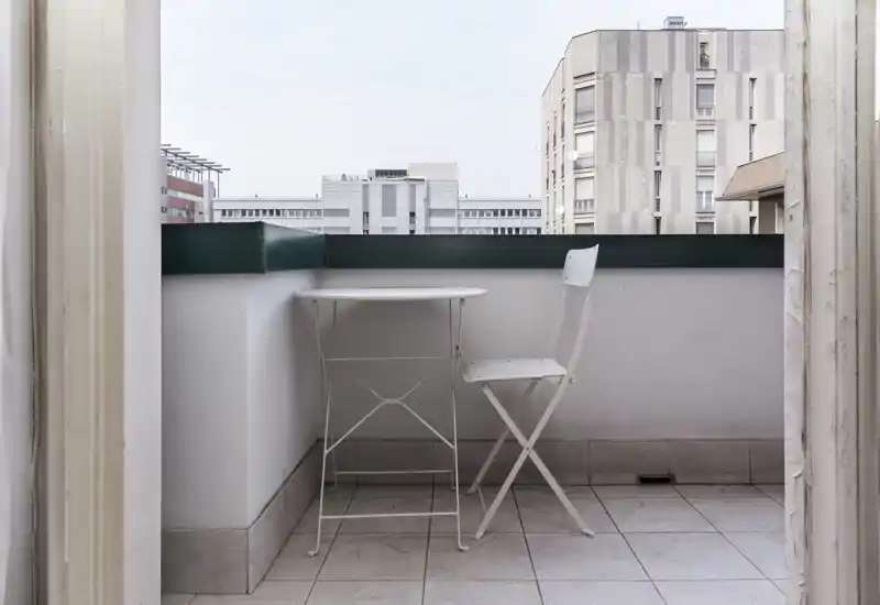 Small urban balcony with a round bistro table and a folding chair, tiled floor and a city view — ideal for a morning coffee.