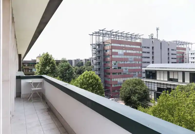 Sunny private balcony overlooking trees and modern office buildings, with a small folding table and chair — ideal for morning coffee or relaxing outdoors.