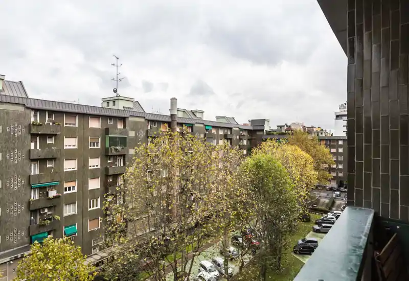 View from a balcony overlooking a courtyard and neighboring apartment blocks with trees and parked cars; overcast sky provides soft, even light.