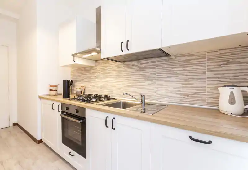 Bright, modern fitted kitchen with white cabinets, wood-effect countertop and tiled splashback, featuring a gas hob, built-in oven and stainless sink — ideal for compact apartment listings.