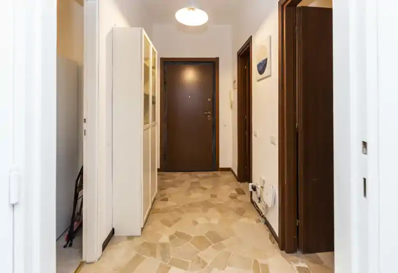 Bright and tidy entrance hallway with a wooden front door, tiled floor and built-in storage cabinet — a welcoming first impression.
