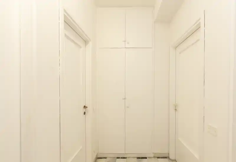 Ingresso stretto e luminoso con porte bianche simmetriche e un armadio a muro; pavimento a piastrelle chiaro e palette neutra.