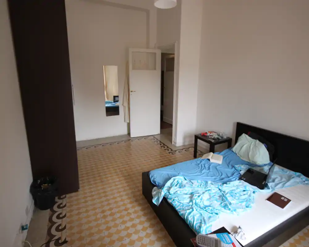 Chambre lumineuse et minimaliste avec lit bas double, table de chevet et sol carrelé décoratif. La lumière naturelle et le mobilier simple offrent une atmosphère calme, adaptée aux annonces.