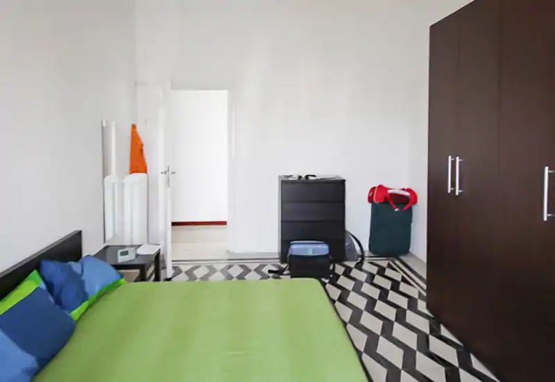 Chambre lumineuse et simple avec housse de couette verte, oreillers colorés et grande armoire foncée; sol carrelé graphique qui apporte du caractère.