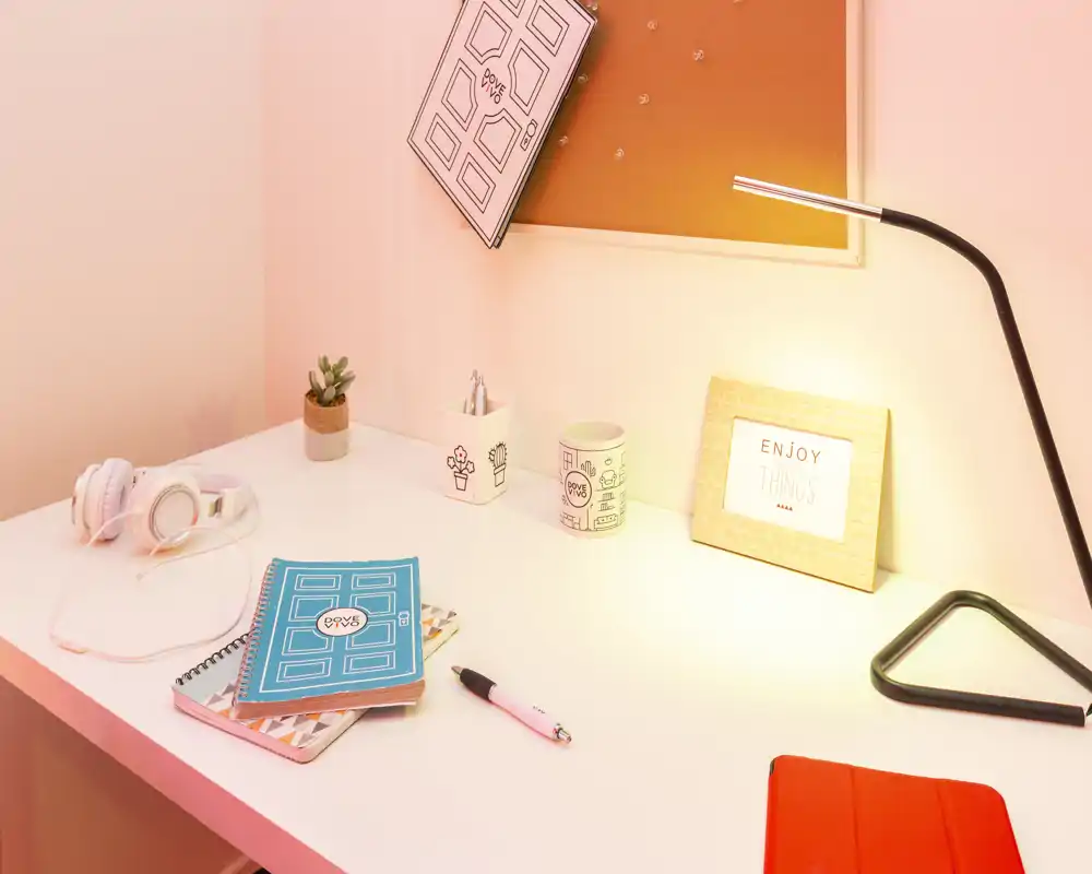 Escritorio luminoso y ordenado con cuadernos, auriculares, una pequeña planta y una lámpara — un rincón de trabajo acogedor ideal para estudiar o teletrabajar.