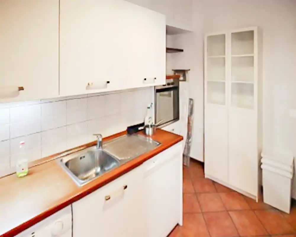 Cucina compatta con mobile bianchi, doppio lavello e piano in legno; pavimento piastrellato e forno incassato per una soluzione funzionale.