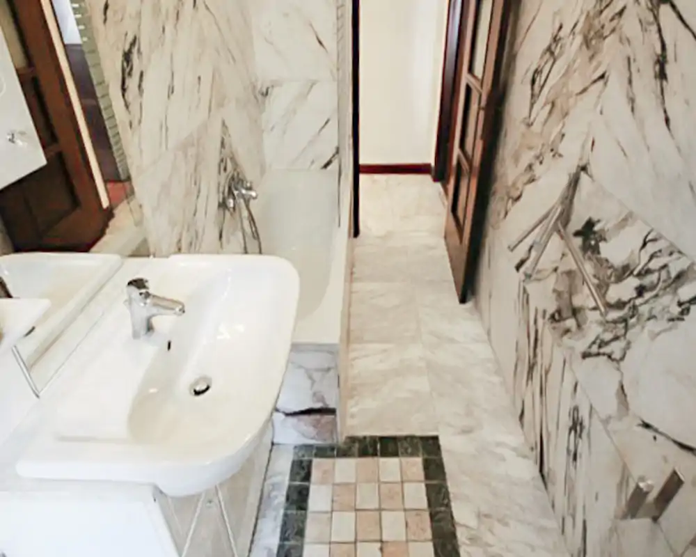 Bagno luminoso con finiture in marmo, dotato di lavabo, vasca e pavimento piastrellato; finiture classiche e specchio ampio sopra il lavabo.