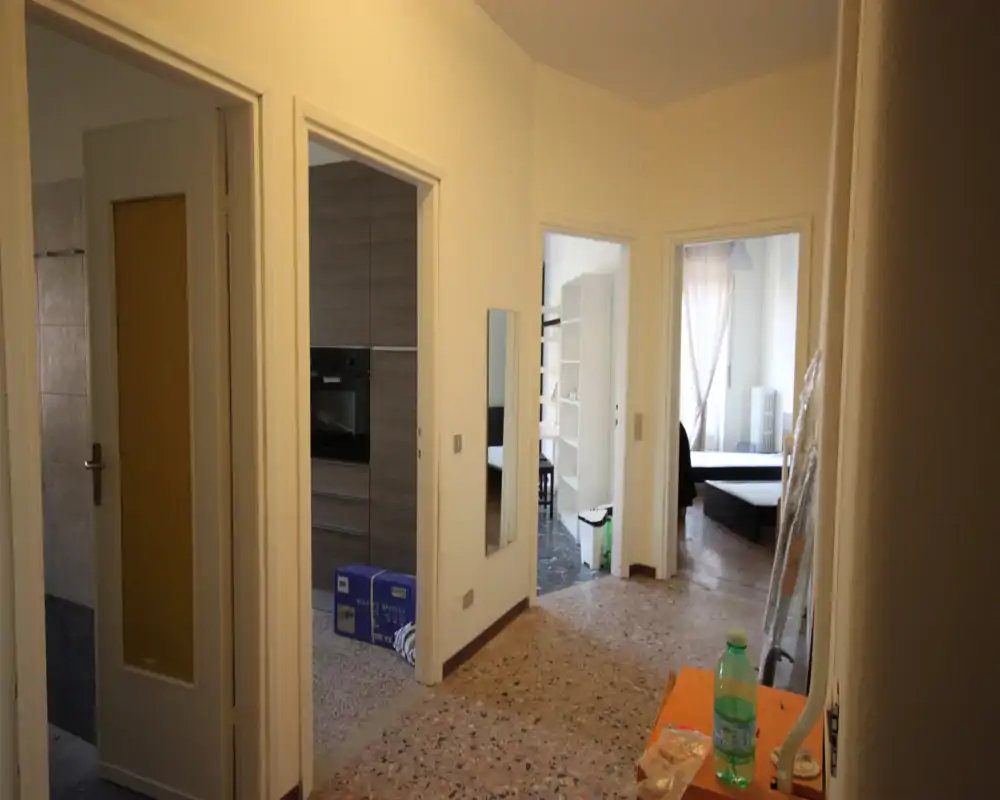 Entry hallway with multiple doorways leading to kitchen and bedrooms; terrazzo floor and neutral walls give a clear view of the apartment layout.