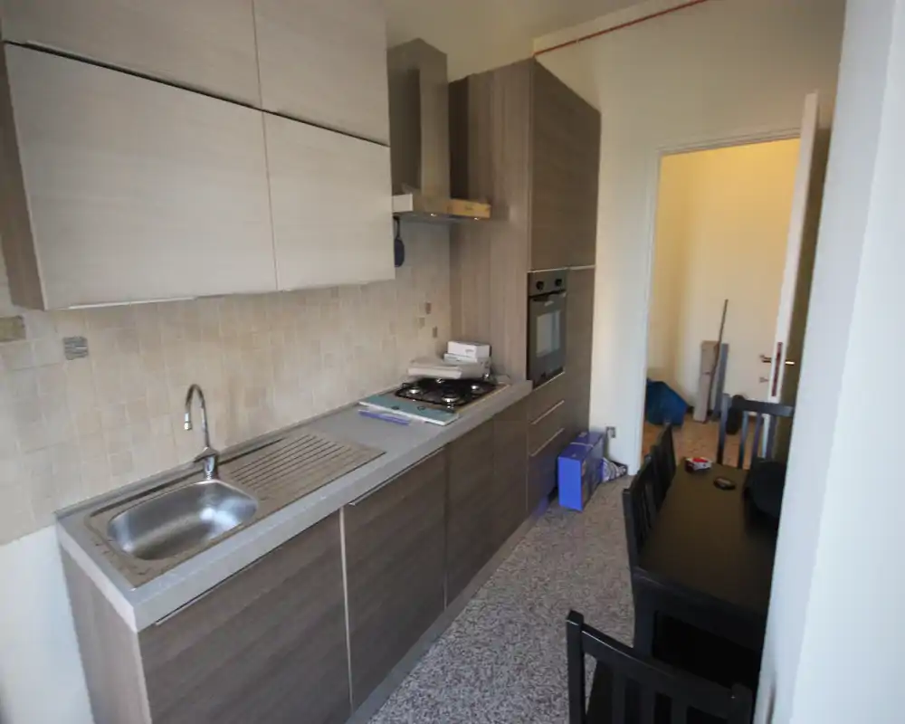 Narrow galley kitchen with modern wood-effect cabinets, integrated oven and gas hob, stainless sink and small dining table—functional layout ideal for compact apartments.